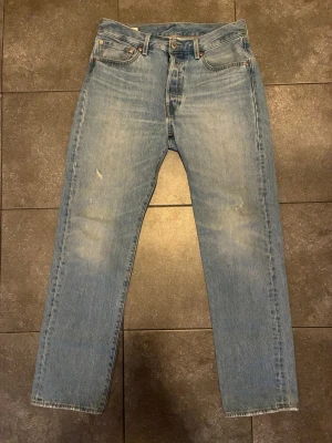 Levi's ljusblå 501 - Säljer ett par klassiska ljusblå jeans från Levi's med rak passform och fem fickor. Jeansen har en vintage tvätt och den ikoniska läderlappen bak i midjan. Passar perfekt för en avslappnad look.