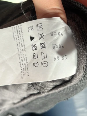 Grå chinos från Hugo boss  - Snygga grå chinos från Hugo boss med klassisk passform och diskret logga ovanför bakfickan. Byxorna har bälteshällor, två bakfickor och är tillverkade i ett mjukt, vävt material som känns bekvämt hela dagen.