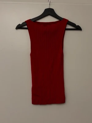 Röd ribbad ärmlös topp - Snygg röd ärmlös linnetopp med ribbad struktur. Toppen har en rak halsringning och är figurnära i modellen, perfekt att styla med jeans eller kjol. Enkel och stilren design som passar till många olika looks.