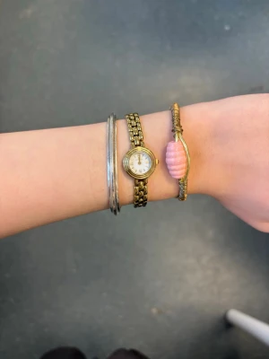 Guldigt armband med rosa pärla - Handgjort armband💕 Unikt armband i guldfärgad metall med en tvinnad design och en stor, räfflad rosa pärla i mitten. Armbandet har öppna ändar med dekorativa snurror och inslag av lindad metalltråd för en cool, handgjord känsla.