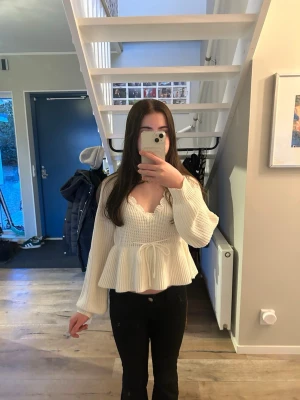 Krämvit stickad peplumtröja - Söt krämvit stickad tröja med peplumvolang och djup v-ringning med vågig kant. Tröjan har långa ärmar med ribbade muddar och knytband i midjan. Perfekt för en trendig och feminin look. Storleken är M men passar mig som vanligtvis bär XS. Pris kan diskuteras.💗 
