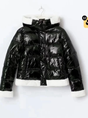 Svart glansig pufferjacka med fuskpäls - Snygg svart glansig pufferjacka med vit fuskpäls på huva, ärmslut och nederkant. Jackan har dragkedja och tryckknappar framtill samt två sidofickor. Perfekt för kalla vinterdagar och ger en trendig look. Storlek L men passar för mig som har vanligtvis storlek S🫶🏻