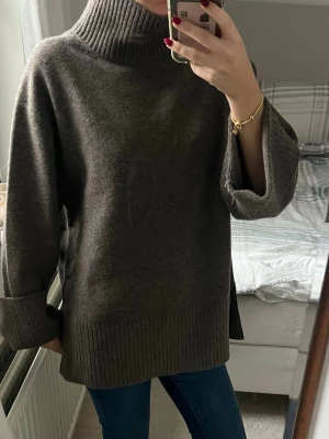 Oversized stickad polotröja - Säljer en oversized stickad polotröja med bred ribbad krage, muddar och nederkant. Den har en brun/grå färg. Tröjan har vida ärmar och en avslappnad passform, perfekt för lager på lager. Materialet känns mjukt och tjockt, vilket gör den extra mysig.