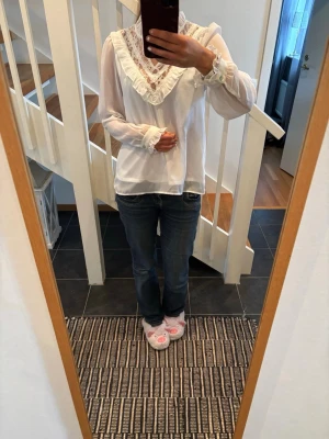 Vit blus med spets och volang - Söt vit blus med långa ärmar, spetsdetaljer och volang runt V-ringningen. Transparenta ärmar och dekorativa knappar vid ärmsluten, ifrån Vila i storlek S och knappt använd!🥰