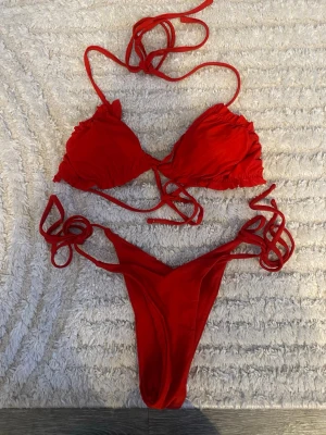Röd bikini med knytband - Snygg röd bikini med trekantsöverdel och knytband både i nacken och ryggen. Underdelen har höga skärningar och knyt i sidorna toppen kan knytas på olika sätt, endast testad 