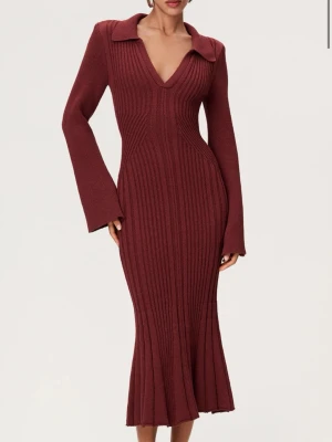 Adoore sandrio klänning - Säljer en vinröd stickad långklänning från adoore med ribbad struktur, v-ringning och bred krage. Klänningen har långa ärmar och markerad midja för en snygg siluett. Perfekt för dig som vill ha en elegant och trendig look.