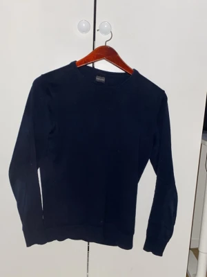 Mörkblå stickad tröja Dan John - Mörkblå stickad tröja från Dan John med rund halsringning och långa ärmar. Enkel och stilren design som passar perfekt till jeans eller chinos. Tröjan har ribbstickade muddar vid ärmslut och nederkant för en snygg passform. Storlek Small men sitter mer som en xs