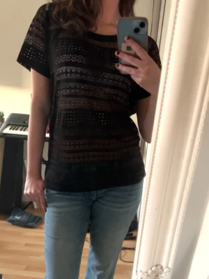 Svart spetsblus  - Säljer en svart transparent blus med korta ärmar och snyggt geometriskt mönster. Blusen har rund halsringning och är tillverkad i ett lätt, syntetiskt material som ger en luftig känsla.💕