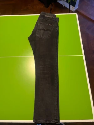 Nudie Jeans, Grim Tim Dark Cove - Säljer ett par svarta  Nudie Jeans i suveränt skick,  med klassisk femficksdesign och raka ben. Jeansen har en diskret logga på bakfickan och är tillverkade i mjukt denimtyg. De är storlek 30 i midja och 30 i längd. Pris går att diskuteras.