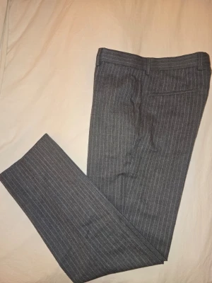 Bläck kostymbyxor – Grårandiga tailored - Bläck kostymbyxor – Grårandiga (48, Tailored Fit) Grårandiga kostymbyxor från Bleck. Storlek: 48 Passform: Tailored Fit Skick: Bra begagnat skick.