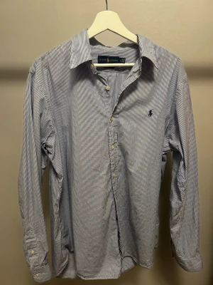 Randig skjorta från Ralph Lauren - Klassisk skjorta från Ralph Lauren med smala blå och vita ränder. Storlek L men passar även stor M