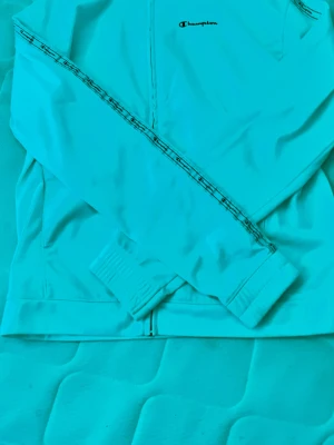 Vit ziptröja från Champion - Säljer en vit ziptröja från Champion med logga på bröstet och snygga band med mönster längs ärmarna. Tröjan har hög krage, muddar vid ärmslut och nederkant samt fickor på sidorna. Perfekt för en sportig och avslappnad stil.storleken känns ganska mycket mindre mer som m.