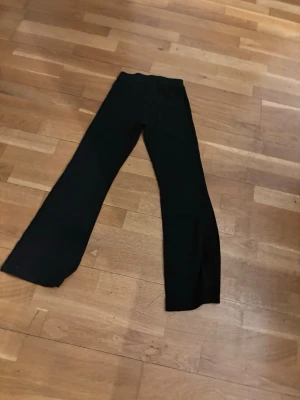 Svarta ribbade leggings med utsvängda ben - Säljer ett par svarta leggings med ribbad struktur och utsvängda ben. De har hög midja och är stretchiga för en bekväm passform. Perfekta att styla med en oversized hoodie eller crop top.