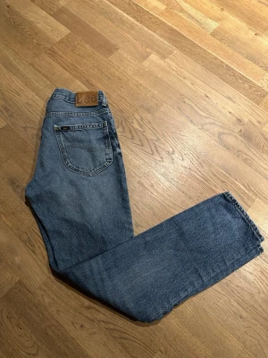 Blå raka jeans från Lee - Säljer ett par klassiska blå jeans från Lee med rak passform och fem fickor. Jeansen har en snygg vintage tvätt och Lee-lapp bak i midjan. Tillverkade i slitstark denim, perfekta för en avslappnad och tidlös stil.                  Nypris: 1200