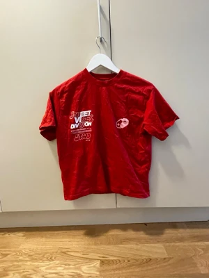 Röd Street Vibes Division t-shirt - Cool röd t-shirt från Street Vibes Division med tryck både fram och bak. T-shirten har korta ärmar, rund hals och är gjord i mjuk bomull. Perfekt för dig som gillar streetwear och vill sticka ut med ett snyggt tryck.