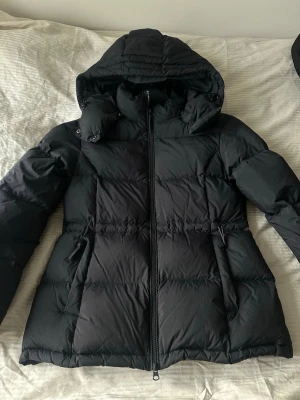 Svart GANT jacka  - Snygg svart pufferjacka med stor huva och dragkedja framtill. Jackan har två sidofickor med dragkedja och en innerficka. Passar XS också, använd fåtal gånger 