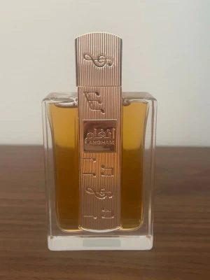 Angham exklusiv parfymflaska - Snygg parfymflaska från Angham med guldfärgat lock och detaljer i metall. Flaskan är rektangulär i genomskinligt glas och innehåller en bärnstensfärgad vätska. 