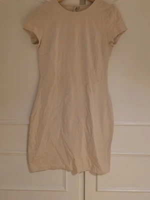 Beige kortärmad klänning - En stilren beige kortklänning med rund halsringning och korta ärmar. Klänningen har en enkel och figurnära passform. Aldrig använd. Klänningen är ifrån kollektion med Bianca som jade samarbete med Nelly. Säljer två av dessa klänning.