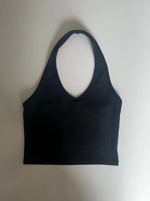 Svart ribbad halterneck topp - Säljer en svart ribbad halterneck topp från Miss Selfridge i storlek 36. Toppen har v-ringning och är ärmlös med croppad passform. 