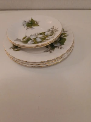 Blommiga assietter med guldkant - Säljer ett set med vita assietter i porslin med gröna och vita blommor samt guldkant runt om Märket royal albert.