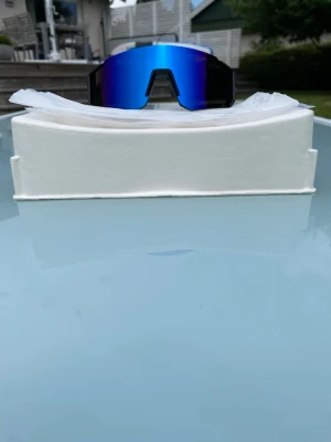 Sportsolglasögon - Hej! Säljer ett par riktigt ”snabba” och snygga sportsolglasögon med spegelglas i nyanserna blå och lila. Såklart UV400: blockerar 100% av skadliga strålar. Design: bekväm lättviktsram för långa pass. Modellen är i populära Sutro stilen med stor lins och ramlös nederkant - utmärkt budgetalternativ som fyller exakt samma funktion, inte Bliz. Passar perfekt för ditt nästa äventyr oavsett om det är på en slingrig stig i Alperna eller på gatan utanför huset! Tveka inte att höra av dig vid frågor!