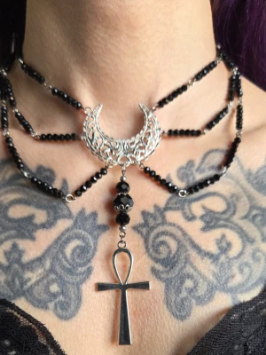 Svart gotiskt halsband med ankh och måne goth bohem moon  - Unikt halsband med svarta pärlor, silverfärgad kedja och detaljer. Smycket har en stor dekorativ halvmåne i metall och ett hängande ankh-kors. Perfekt för dig som gillar alternativ stil och statement-accessoarer. Egendesignat/egenkomponerat.
