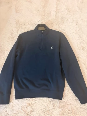 Marinblå halvzip från Polo Ralph Lauren - Snygg marinblå tröja från Polo Ralph Lauren i storlek M, med halv dragkedja och klassisk vit logga på bröstet. 