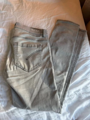 Grå dondup jeans - Säljer ett par grå skinny jeans med flera slitningar och hål på benen för en riktigt edgy look. Jeansen har klassisk femficksmodell och är tillverkade i ett stretchigt denimtyg som sitter tajt. Perfekta för dig som gillar streetstyle och vill sticka ut.