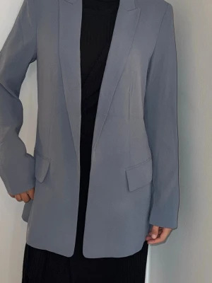  kavaj - Snygg ljusgrå kavaj med rak passform och klassiska slag. Kavajen har två fickor med lock framtill och är helfodrad. Perfekt för en stilren och modern look. Materialet känns mjukt och har en lätt struktur. OBS! Modellen är XS och bär storlek S (38)
