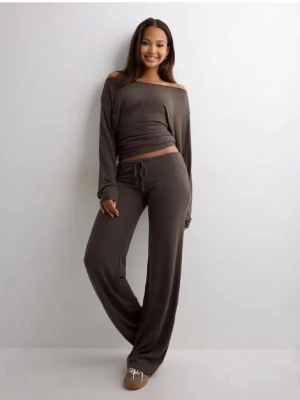 Nelly chill pants - Mysigt loungewear-set i mjukt brunt tyg med långärmad topp med off-shoulder och vida byxor med dragsko i midjan. Perfekt för chill dagar hemma. Materialet ser stretchigt och bekvämt ut.