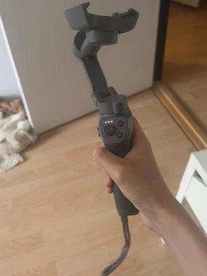 Grå gimbal för smartphone - Säljer en grå gimbal för smartphone, perfekt för att stabilisera videoinspelningar och ta snygga bilder. Ergonomiskt handtag med flera knappar för enkel styrning. Tillverkad i plast och metall, kompakt och smidig att ta med.