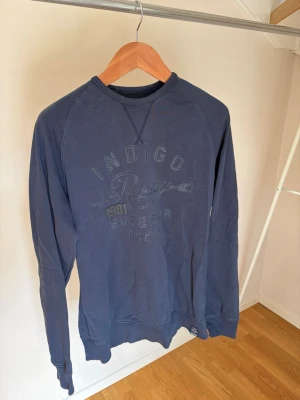 Mörkblå sweatshirt med tryck - Mörkblå sweatshirt med rund halsringning och tryck framtill i samma ton. Tröjan har långa ärmar och ribbade muddar vid ärmslut och nederkant. Perfekt för en avslappnad stil.