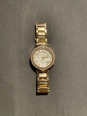 Guldig klocka från Michael Kors - Guldig klocka från Michael Kors med länkarmband i metall och glittrande stenar runt urtavlan. 