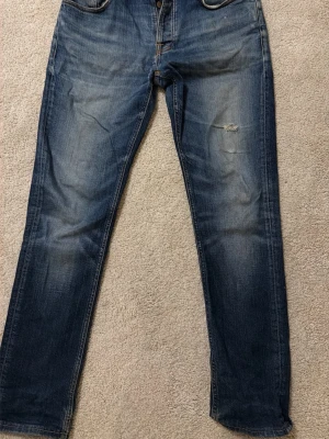 Blå jeans från Nudie Jeans - Säljer ett par klassiska blå jeans från Nudie Jeans med snygg slitning och diskret hål på ena benet. Hör av dig vid frågor☺️