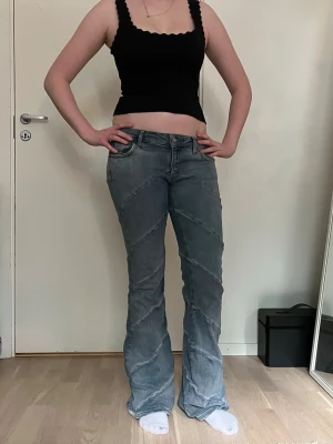 Blå bootcut jeans med snedsydda sömmar - Säljer ett par ljusblå bootcut jeans med snedsydda sömmar och låg midja. Jeansen har klassiska fem fickor och dragkedja med knapp framtill. Snyggt slitna detaljer och unik design som sticker ut.