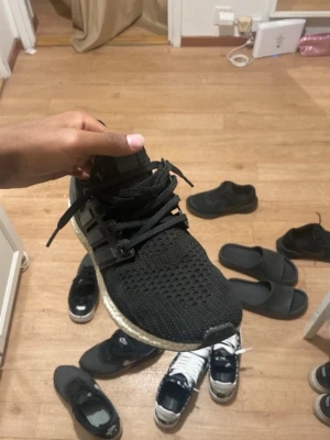 Svarta Adidas Ultra Boost sneakers - Svarta Adidas Ultra Boost sneakers med stickad ovandel och vita Boost-sulor. Skorna har svarta snören och plastdetaljer på sidorna. Perfekta för dig som gillar sportig och clean stil.