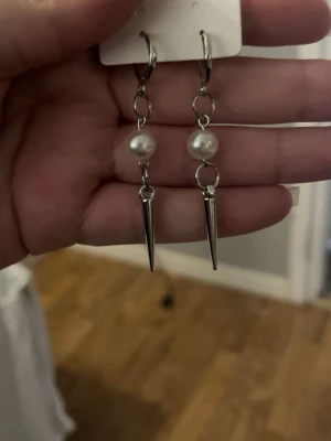 Hemma gjorda Silvriga örhängen med pärlor och spikes - Hemma gjorda Snygga örhängen i silverfärgad metall med vita pärlor och coola spetsiga spikes. Hängande modell med kedjedetaljer som ger en edgy vibe. Perfekta för dig som vill sticka ut med din stil.