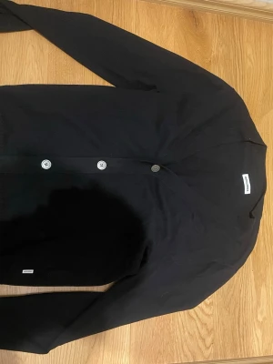 Svart kofta från jack & Jones  - Stilren svart kofta från Jack & Jones. Långärmad modell i mjukt material, perfekt att slänga över en t-shirt eller linne. Enkel och clean design som passar till det mesta.