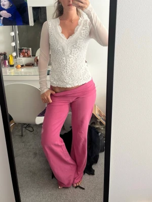 Vit spetsblus med lång ärm - Säljer en vit blus med v-ringning och långa, transparenta ärmar. Toppen har vackra spetsdetaljer och broderat blommönster framtill. 