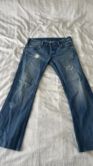 Blå bootcut jeans med slitningar från diesel - Snygga blå bootcut jeans med slitna detaljer på både fram- och baksida. Jeansen har klassisk femficksdesign och en cool tvättad look. Perfekta för dig som gillar en avslappnad och trendig stil.