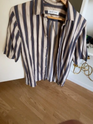Samsoe & Samsoe skjorta - Skjorta från Samsøe Samsøe i modellen Taro NX shirt 10806. Skjortan har korta ärmar och ett randigt mönster i färgerna PUMICE STONE ST. Perfekt till sommaren. Mycket bra skick. Mått kan skickas vid behov.