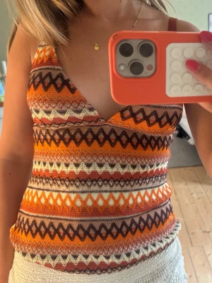 Jättesnyggt Missoni mönstrat linne  - Säljer en färgglad stickad linnetopp med v-ringning och smala axelband. Toppen har ett retroinspirerat mönster i orange, brunt, vitt och beige. Perfekt för dig som vill sticka ut med en unik och somrig vibe. Köpte på en marknad i Frankrike så vet ej märke