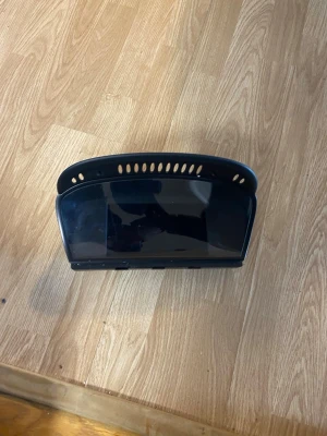 Svart digital bilskärm BMW f10 - En svart digital bilskärm med rundad form och ventilationshål upptill. Skärmen har en blank yta och är troligen till för navigation eller infotainment i bil. Tillverkad i plast och glas, passar till elektronikprojekt eller reservdel.