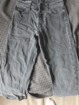 Grå raka jeans från jack and jones - Säljer ett par grå jeans med rak passform och klassisk femficksdesign. Jeansen har normal midja, bälteshällor och dragkedjegylf. Materialet är denim i bomull och färgen är en snygg tvättad grå. Perfekta till en avslappnad stil. W28 L32