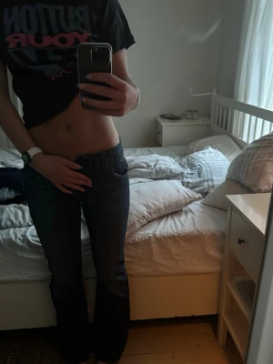 Mörkblå bootcut jeans - Säljer ett par mörkblå bootcut jeans med klassisk femficksdesign och låg midja. Jeansen har kontrastsömmar och en läderpatch bak i midjan. Perfekta för dig som gillar en avslappnad men ändå snygg stil.