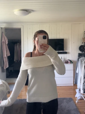 Vit off shoulder stickad tröja - Snygg vit stickad tröja med bred off shoulder-krage och långa ärmar. Tröjan har ribbstickade muddar vid ärmslut och nederkant, vilket ger en stilren och modern look. Perfekt för dig som gillar en avslappnad men trendig stil.