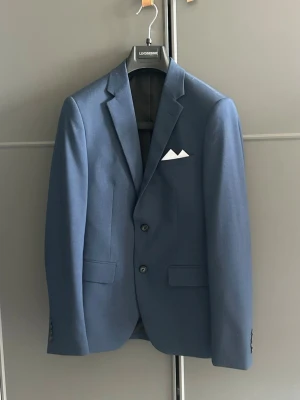 Blå kavaj med ficknäsduk - Snygg blå kavaj med klassisk passform och två knappar framtill. Perfekt för dig som vill ha en stilren och tidlös look. Nypris 1699