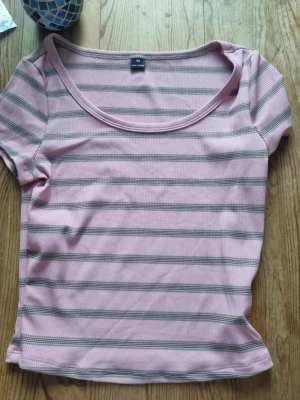 Rosa och grå randig ribbad topp - Säljer en söt rosa topp med gråa horisontella ränder. Toppen har rund halsringning, korta ärmar och är ribbad i materialet för en extra snygg look. Perfekt för dig som gillar en enkel men trendig stil.