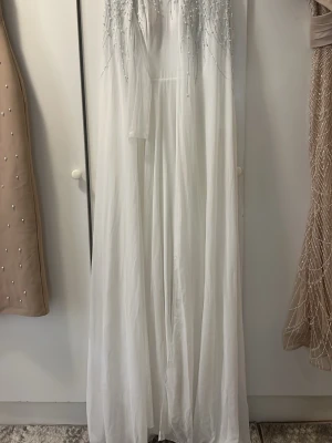 Vit långklänning med pärlor från Faeriesty (SHEIN) - Elegant vit långklänning från Faeriesty med pärl- och paljettdekoration upptill. Klänningen har ett flytande fall och är tillverkad i ett tunt, lätt material som ger en drömmig känsla. Perfekt för speciella tillfällen. Jätte modest