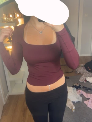 Vinröd långärmad topp med fyrkantig ringning - Säljer en vinröd långärmad topp med snygg fyrkantig ringning. Toppen är tight i modellen och har en croppad passform som framhäver midjan. Perfekt för dig som vill ha en enkel men trendig look.